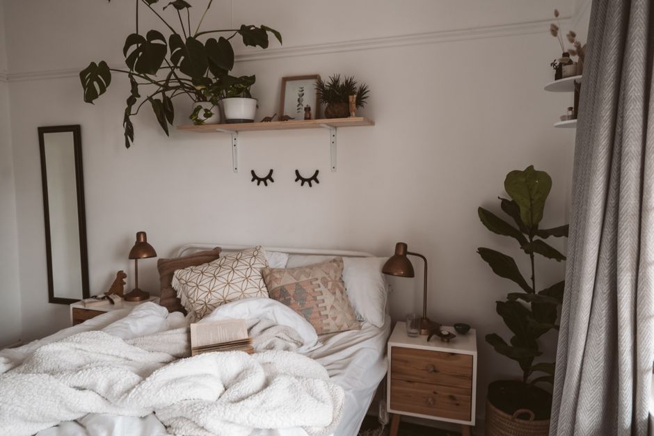 A cozy bedroom with a bench, throw, plant, and warm lighting