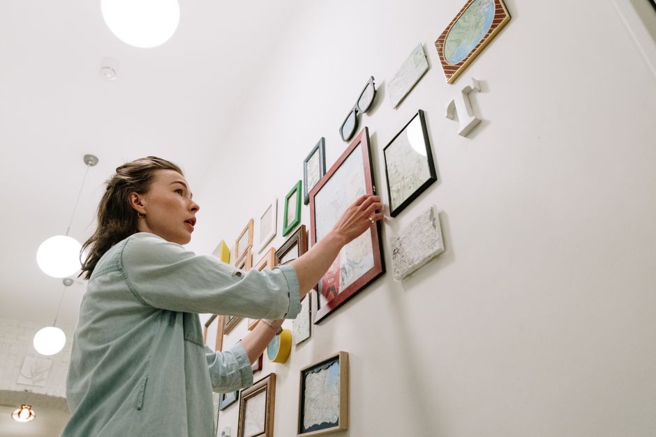 A woman arranging picture frames on a bright indoor wall.
