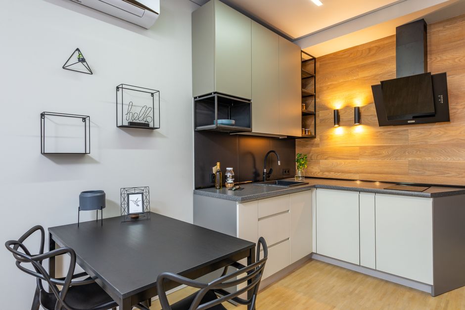 Black table with chairs at decorated wall in modern kitchen with appliances and cupboards near glowing lamps in light apartment