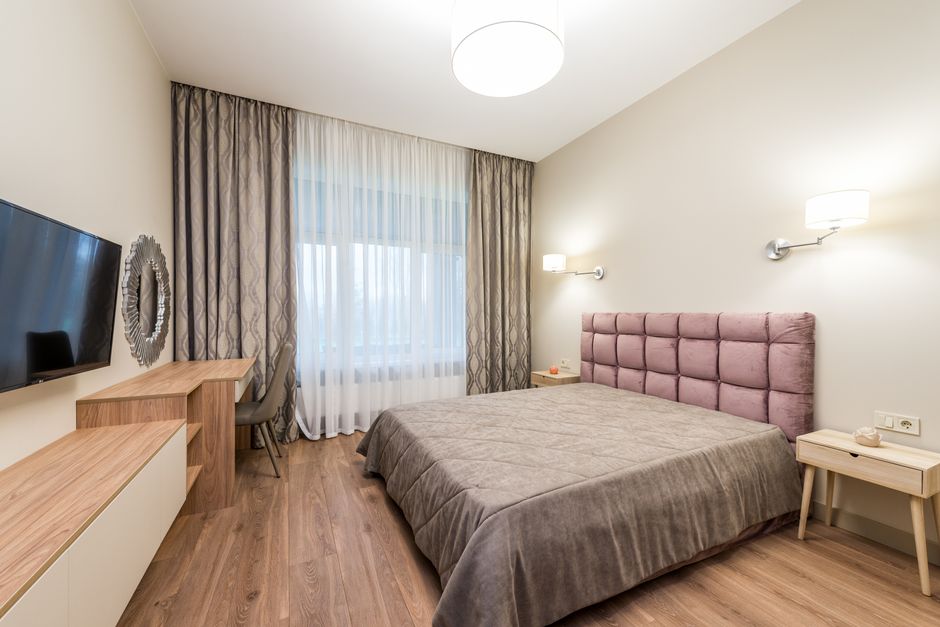 A light neutral bedroom with a mirror and floor-length curtains