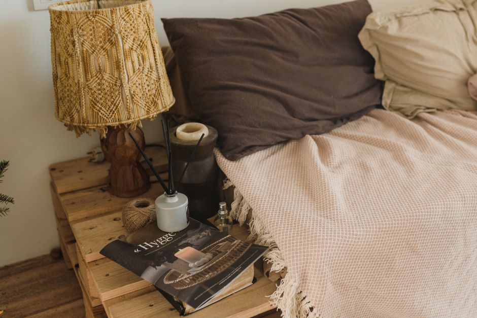 A nightstand styled with a lamp, candle, and stack of books