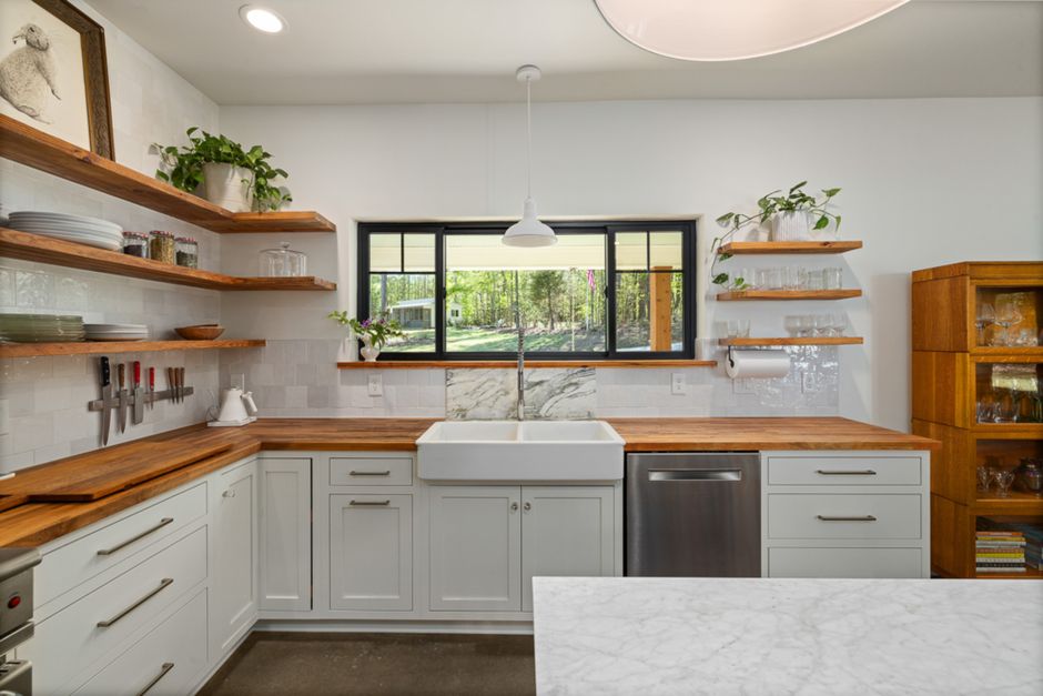 Stylish kitchen featuring open shelving, farmhouse sink, and wooden countertops with a view outside.