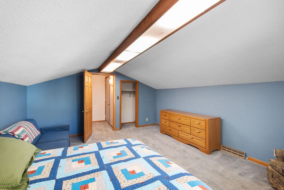 Bright attic bedroom featuring a colorful quilt, wooden dresser, and cozy ambiance.