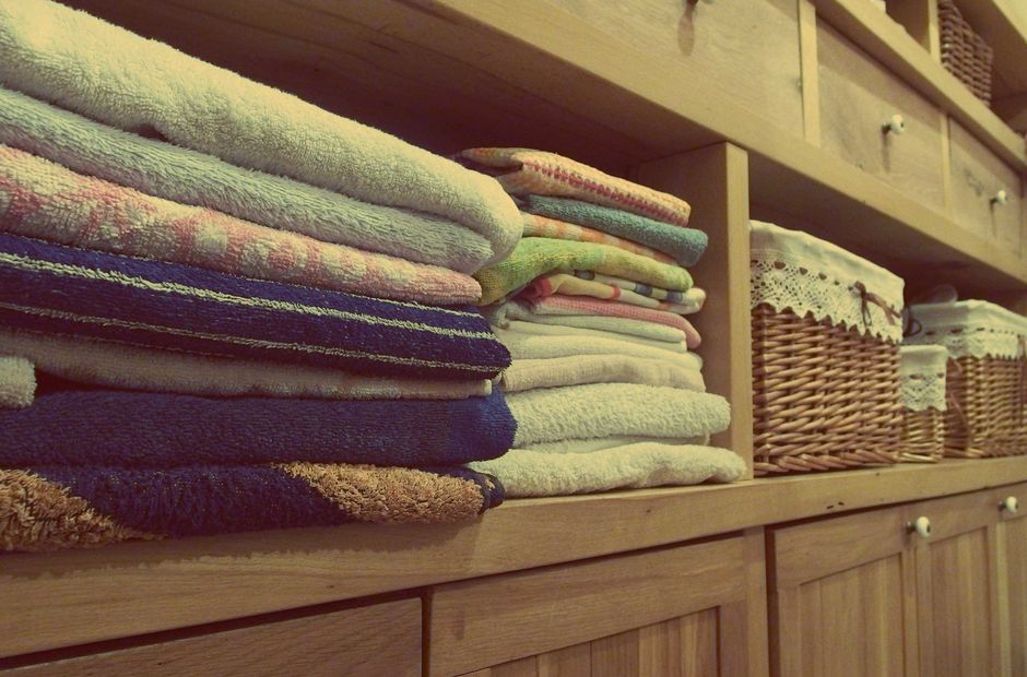 Woven laundry basket beside a stack of neatly folded towels on an open wood shelf