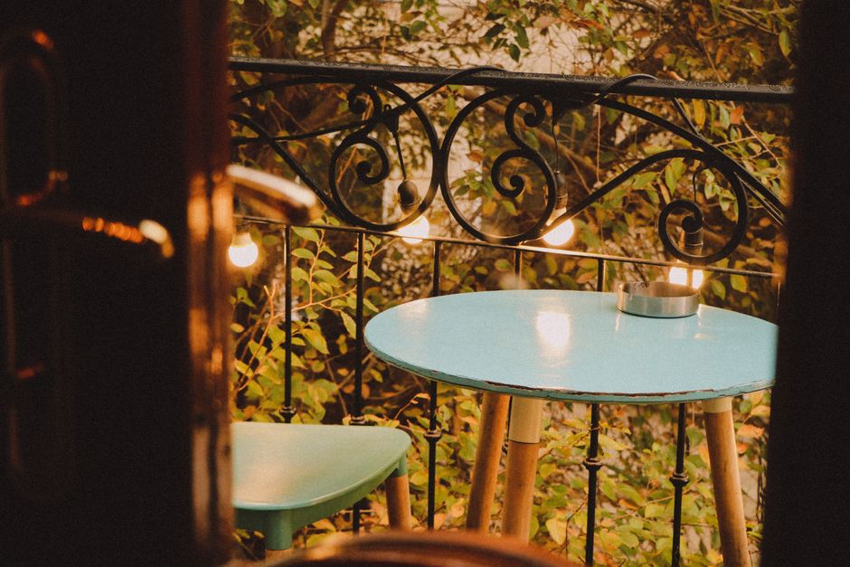 Small apartment balcony with string lights, plants, and a folding chair